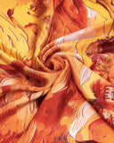 Close-up of a silk scarf featuring an orange and yellow design with a painted pattern, showcasing vibrant colors and texture.
