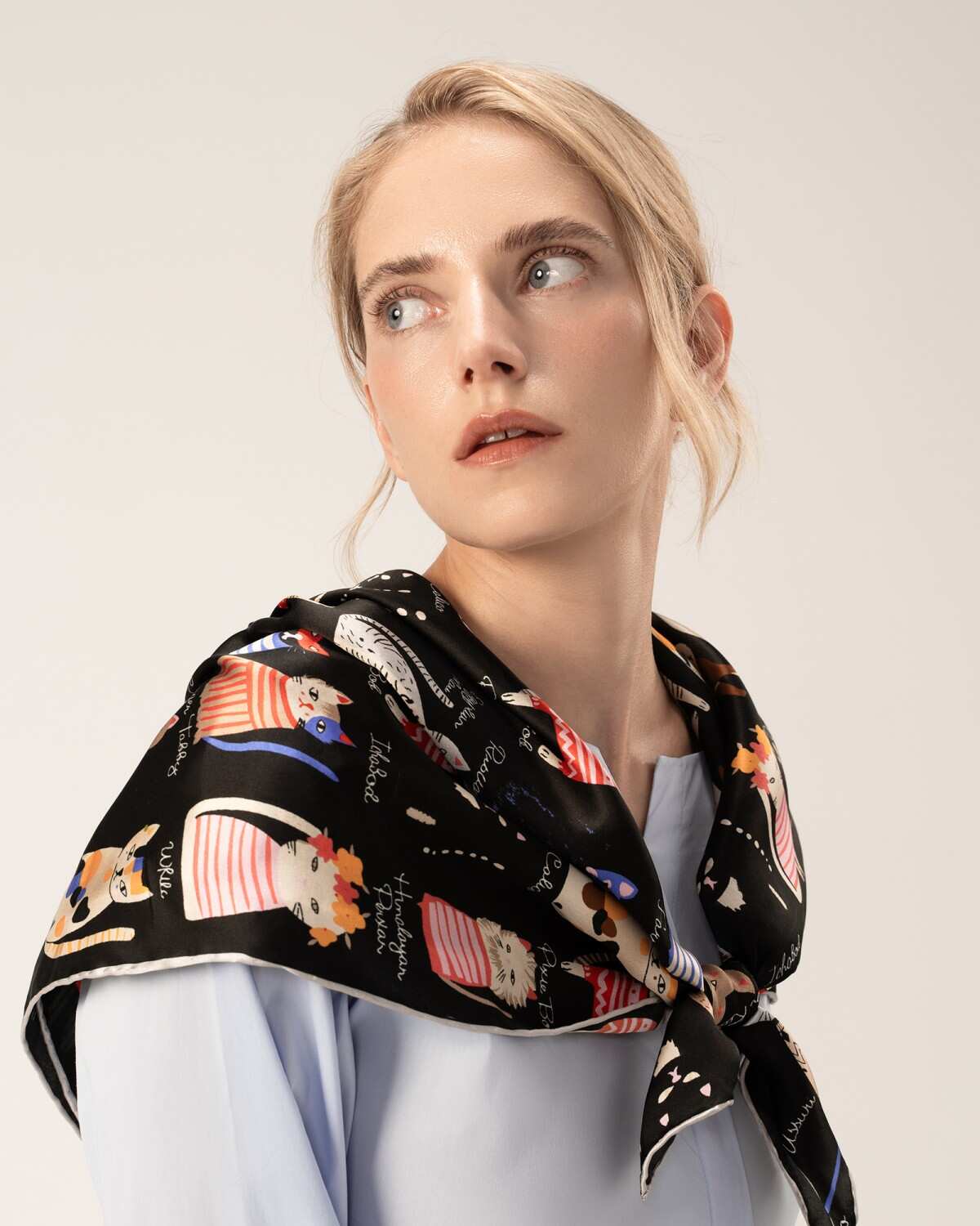A model showcases a silk scarf adorned with cat patterns, elegantly draped over her shoulder in black.