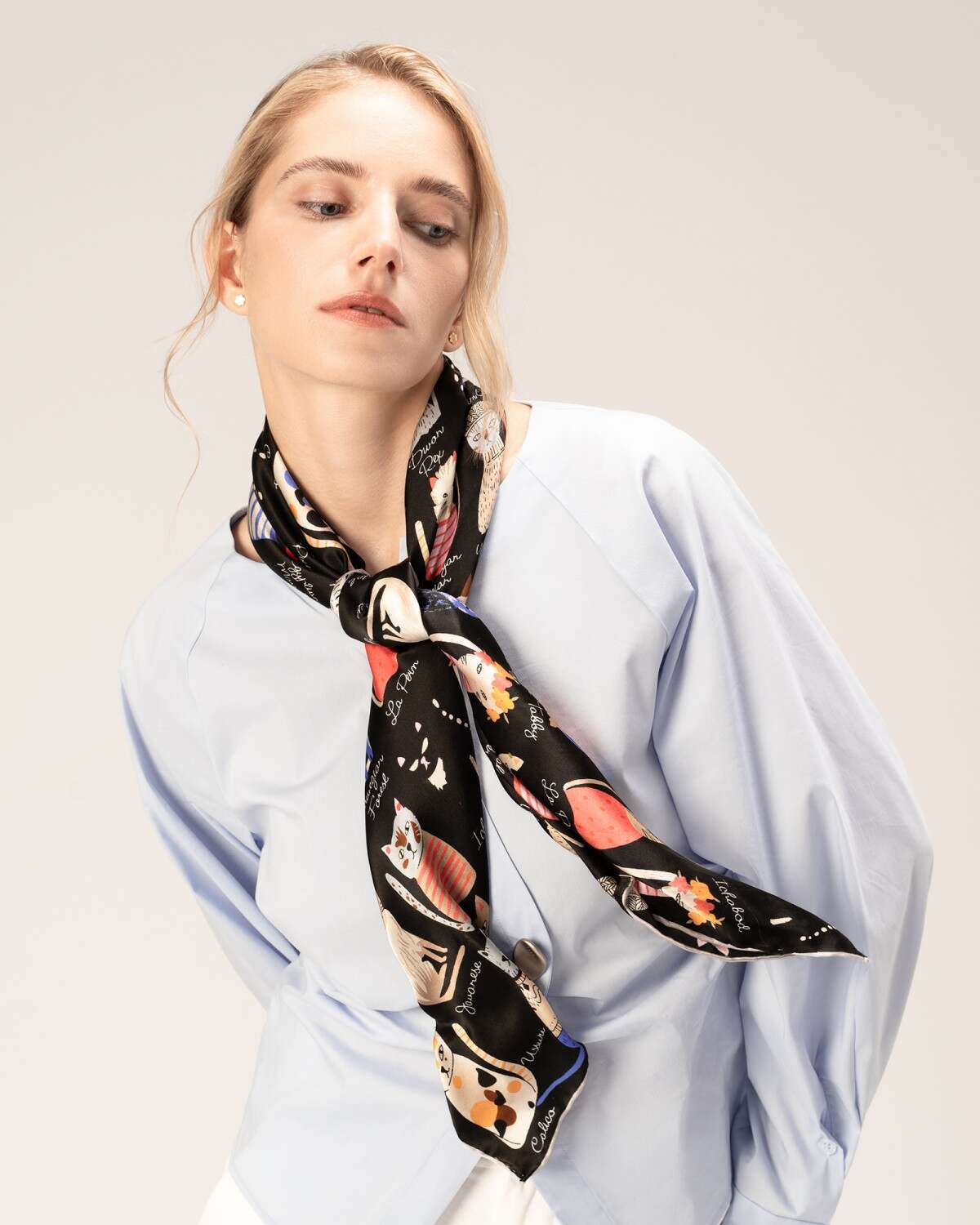 A woman models a blue shirt paired with a luxurious black silk scarf, showcasing elegance and style.