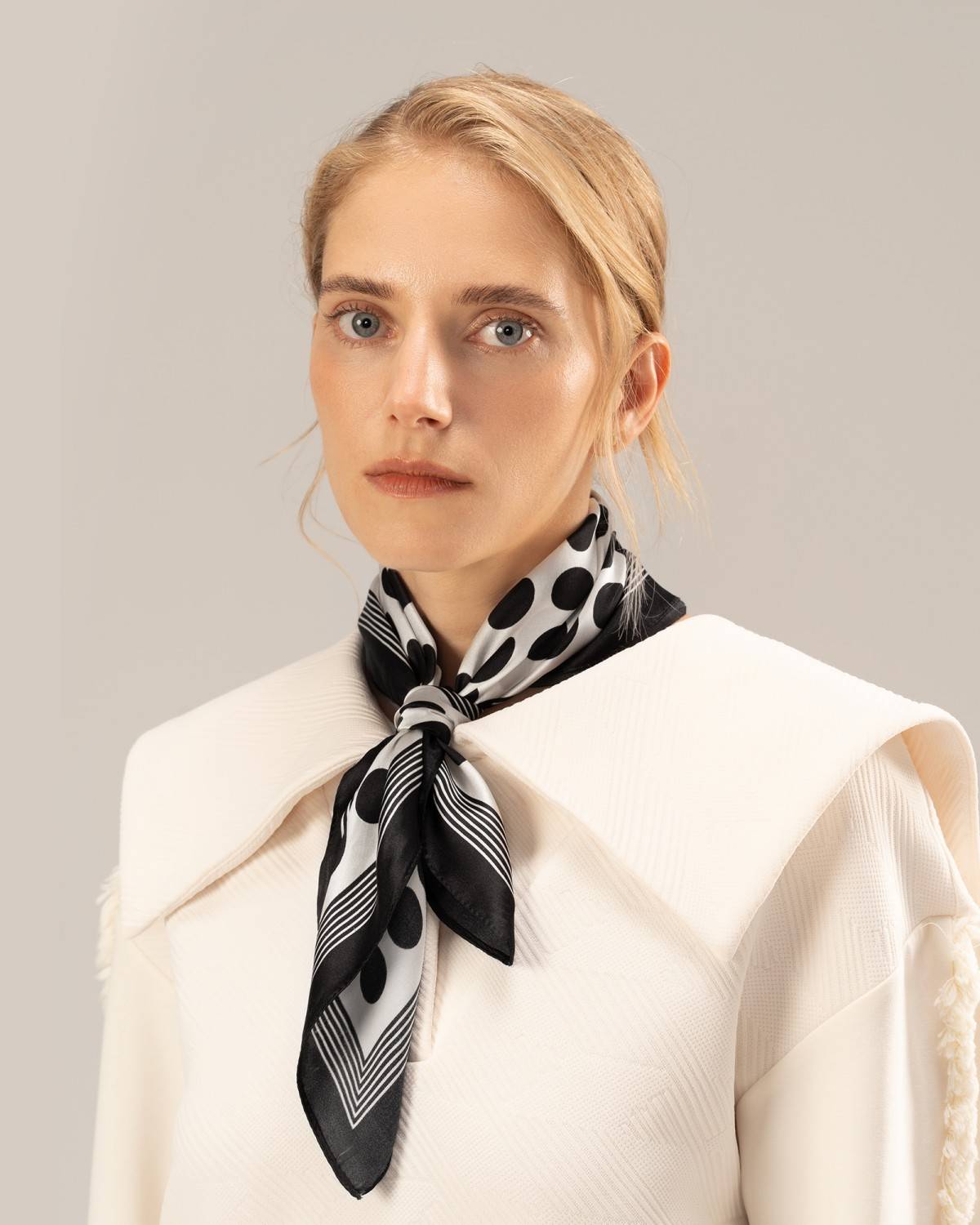 A model wears a white top complemented by a stylish black and white silk scarf around her neck.