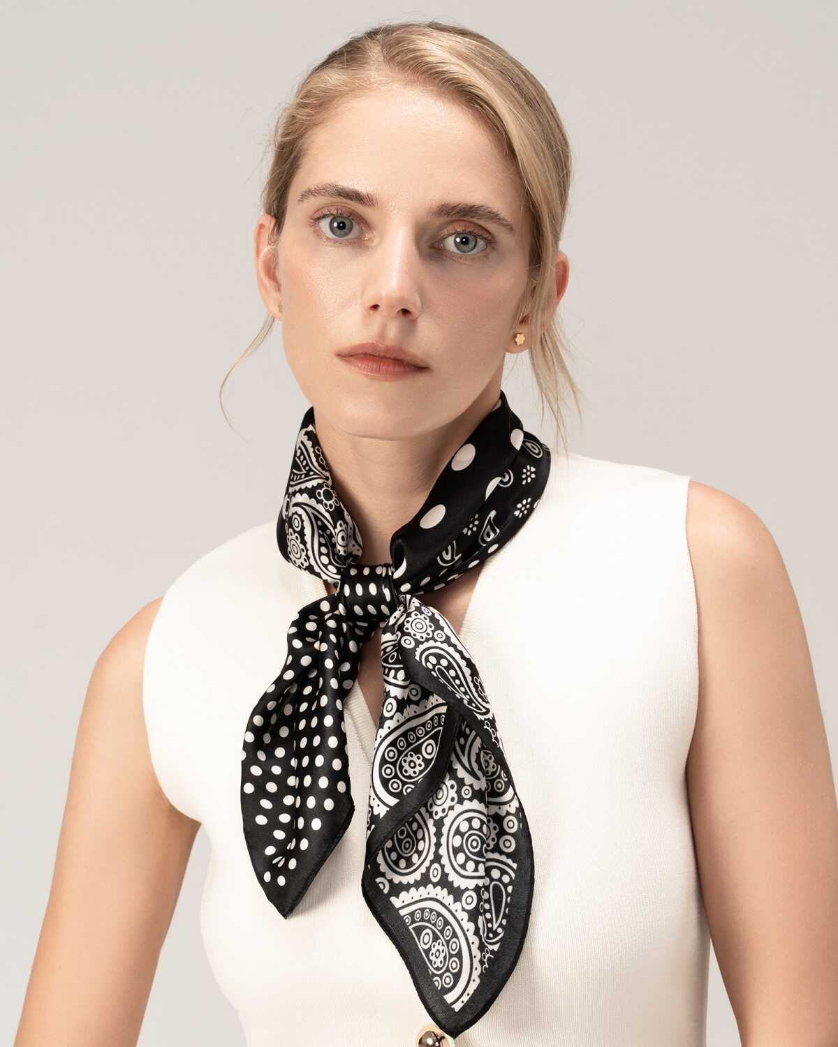 A model showcases a silk scarf featuring a black and white paisley design around her neck.
