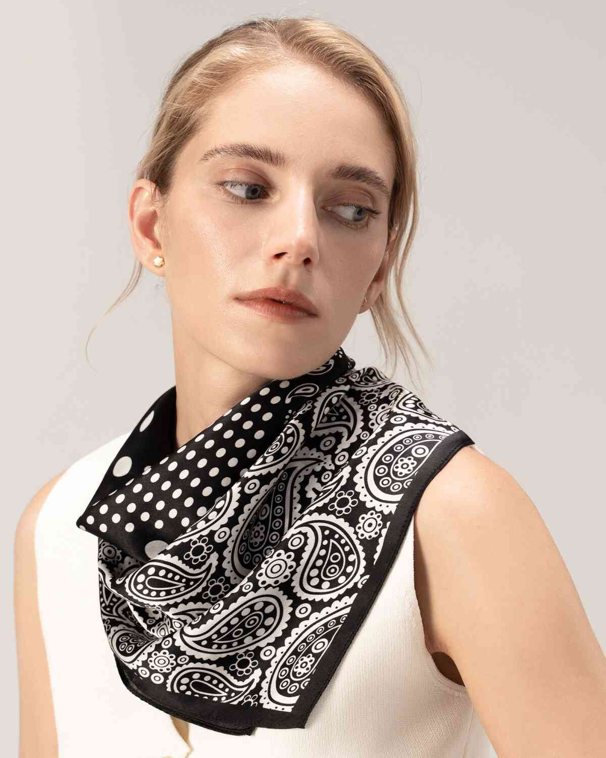 A model showcases a silk scarf featuring a black and white paisley design elegantly draped around her neck.