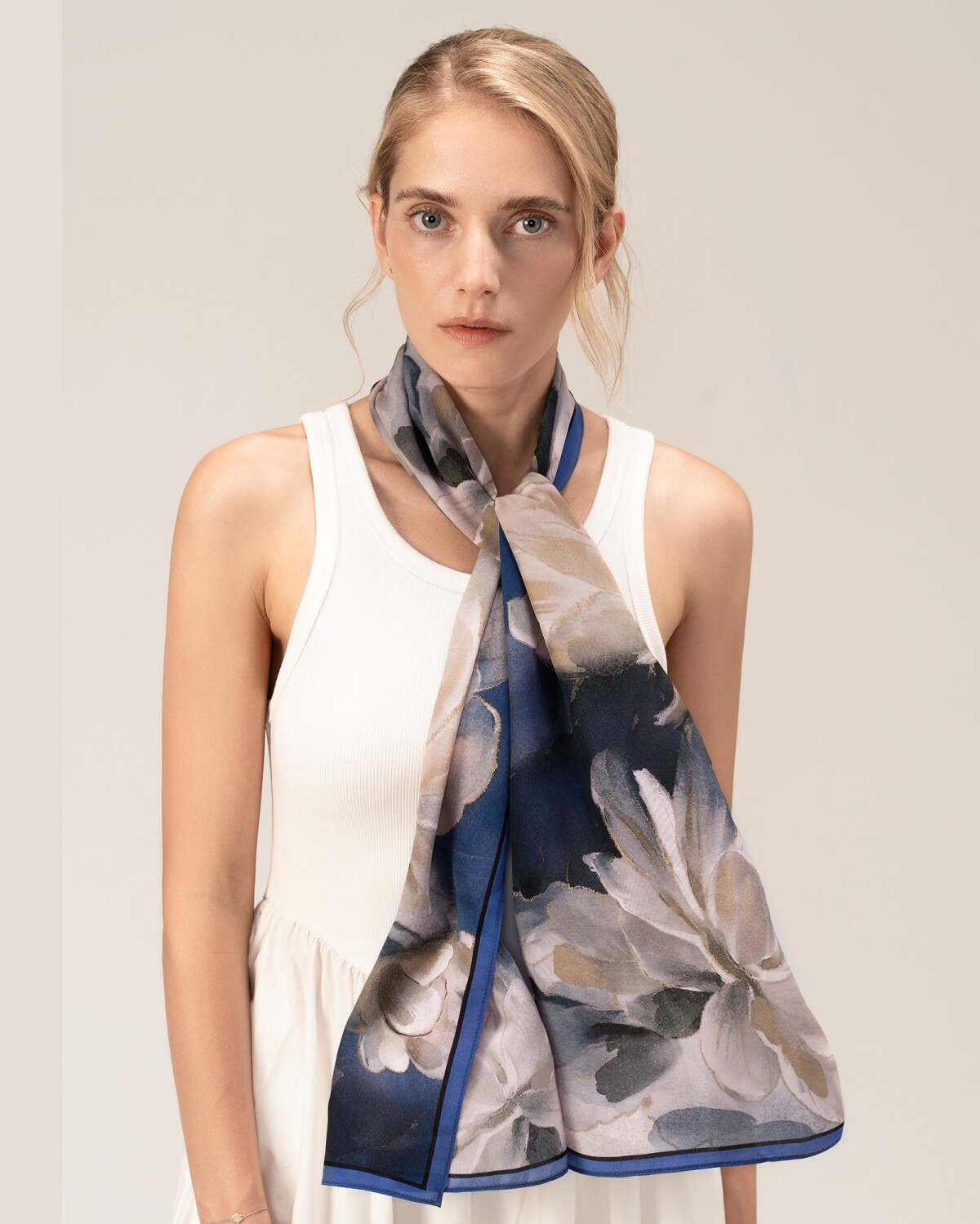 A woman in a white dress adorned with a blue floral print silk scarf, elegantly draped around her neck.