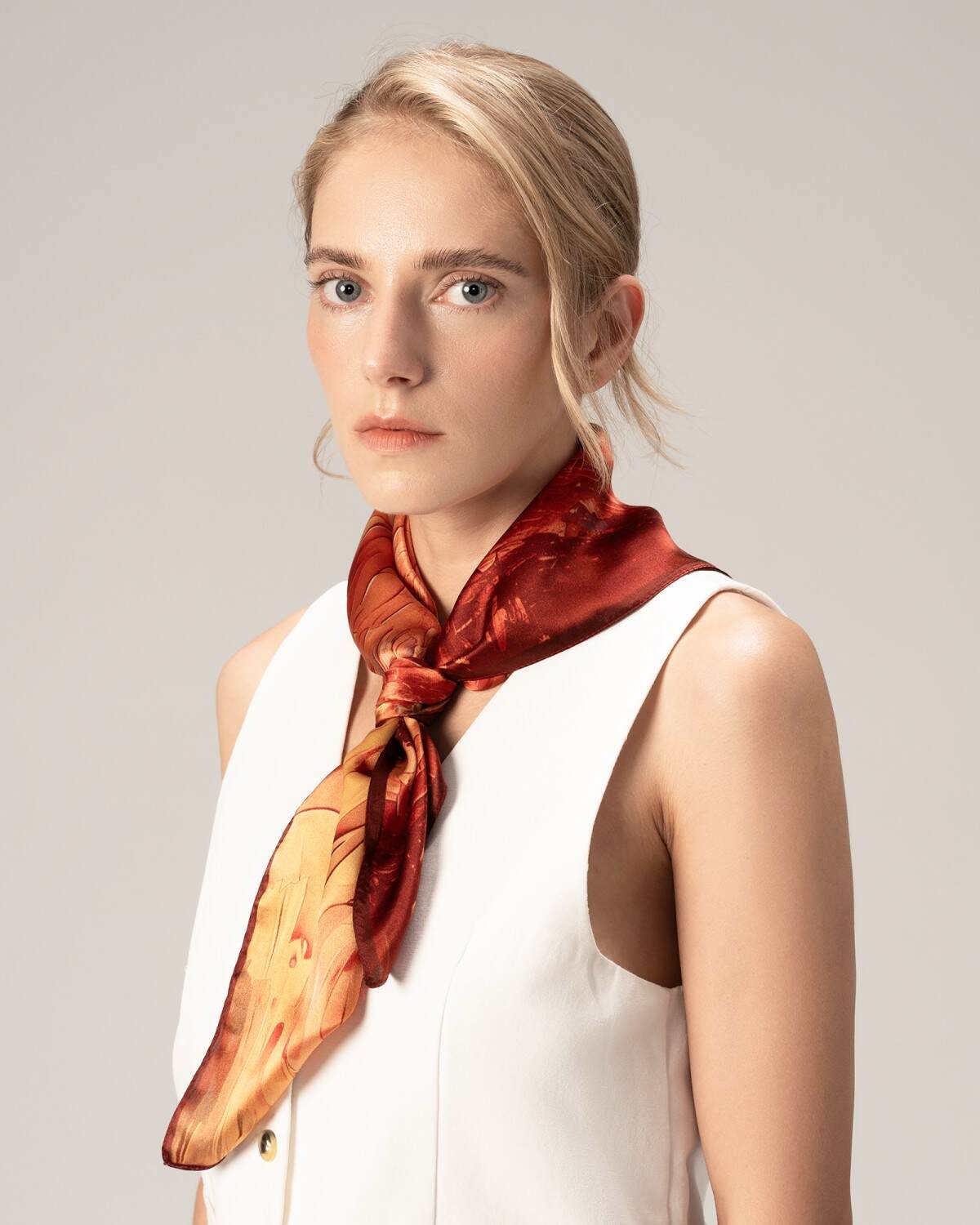 A model showcases a luxurious silk scarf in vibrant red and orange hues, elegantly draped around her neck.