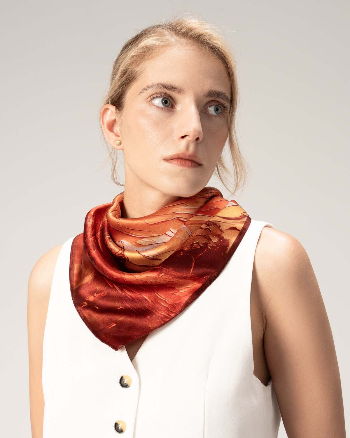 A model displays a silk scarf in bold red and orange colors, adding a touch of elegance to her ensemble.