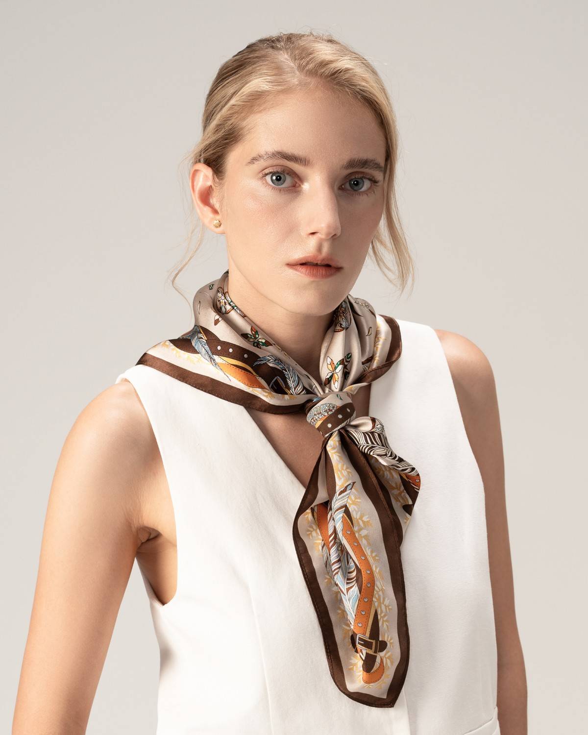 A woman in a white dress adorned with a silk scarf featuring a feather alphabet pattern, posing elegantly as a model.