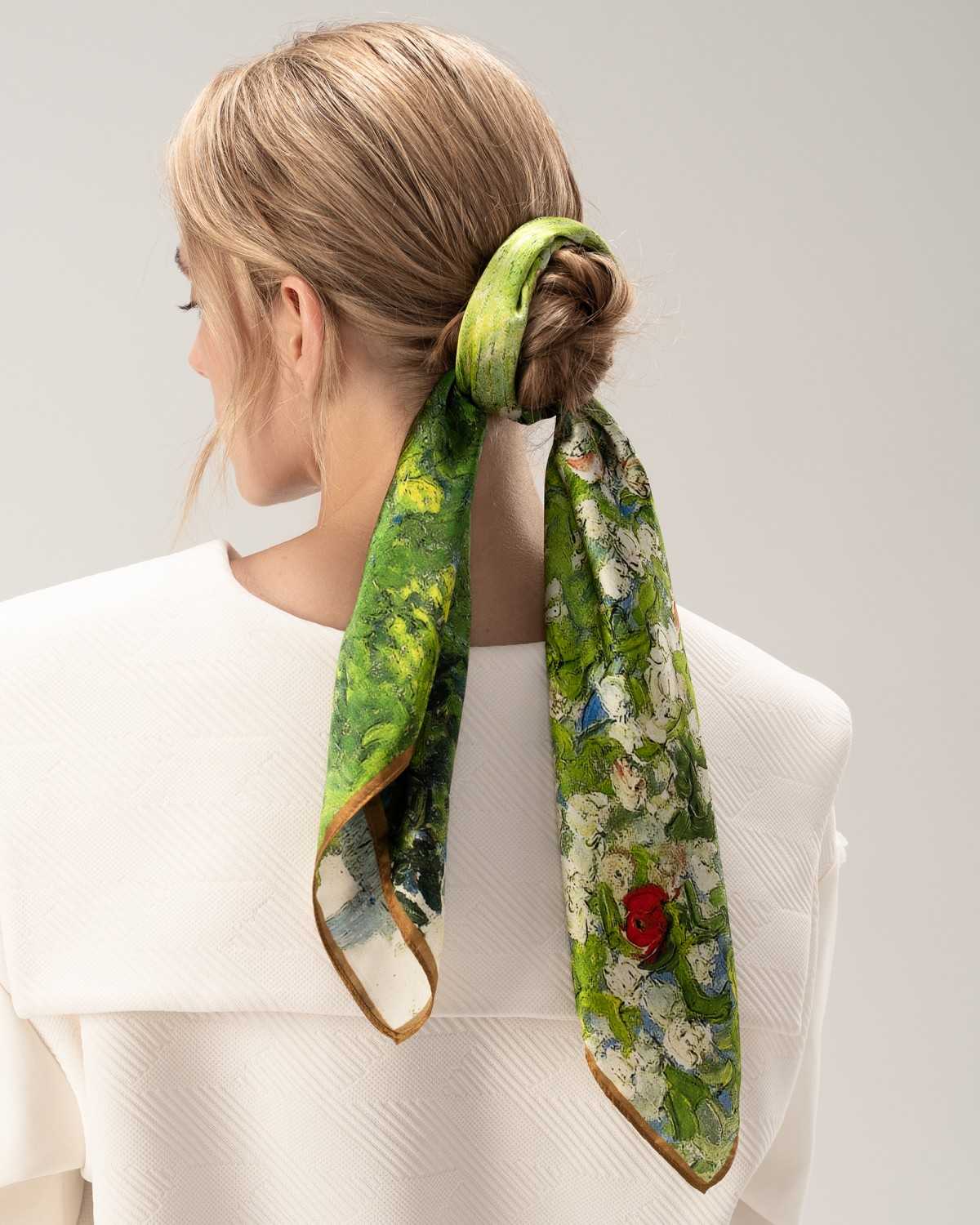 A model showcases a silk hair scarf in green adorned with a vibrant flower pattern, elegantly styled around her head.