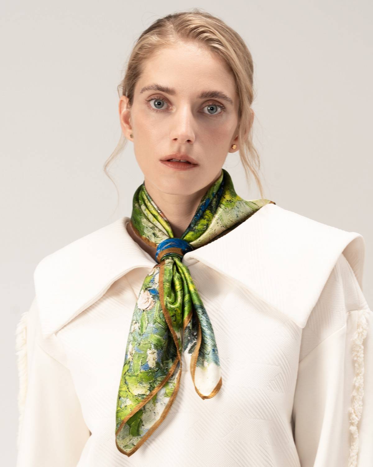 A model elegantly showcases a silk scarf in green and gold, highlighting its luxurious texture and vibrant colors.