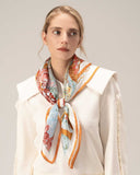 A woman models a white top paired with a vibrant silk scarf adorned in orange and blue patterns.
