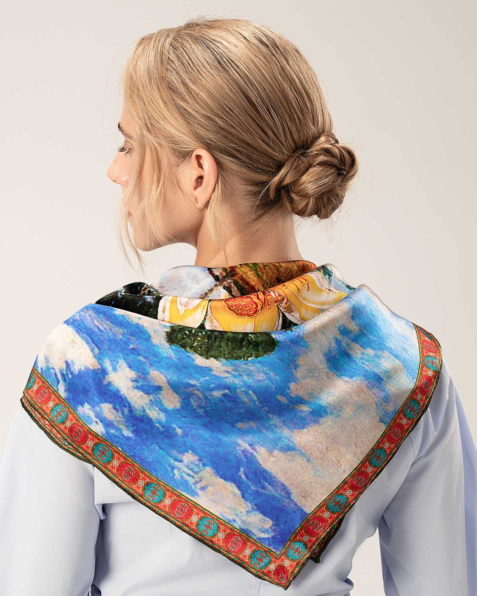 A model showcases a silk scarf adorned with a painting, elegantly draped over her shoulder.