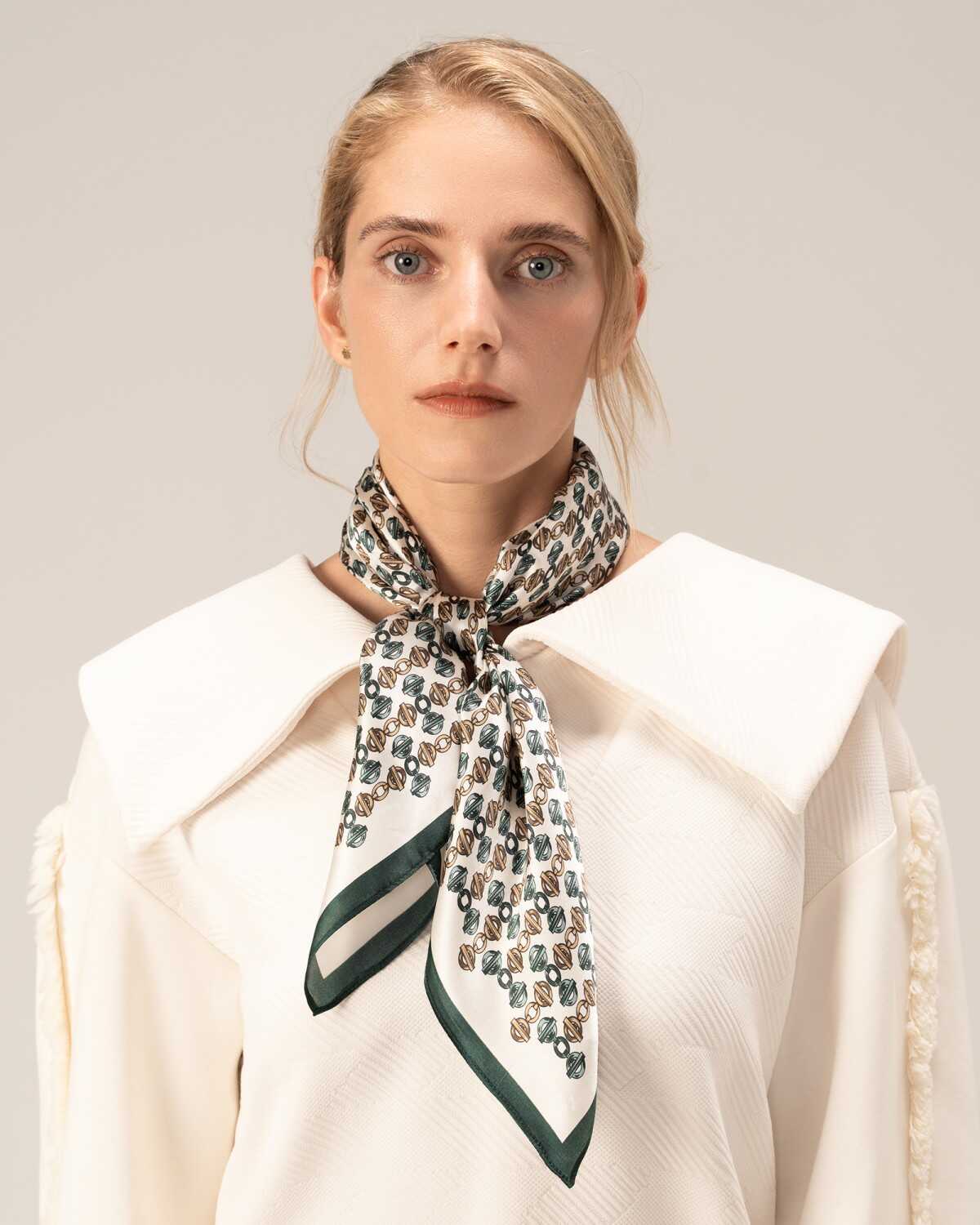 A model in a white shirt elegantly showcases a silk green scarf, highlighting her sophisticated style.
