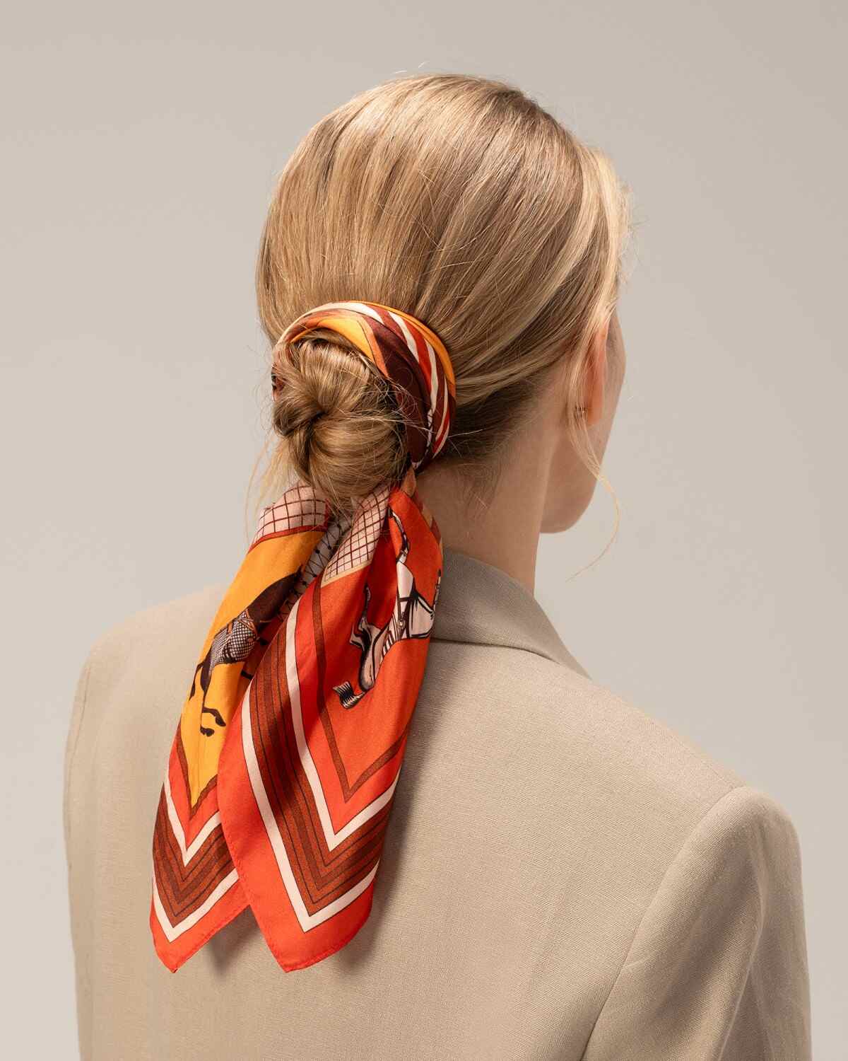 A model wearing a red silk hair scarf and a brown jacket, showcasing a stylish and elegant look.