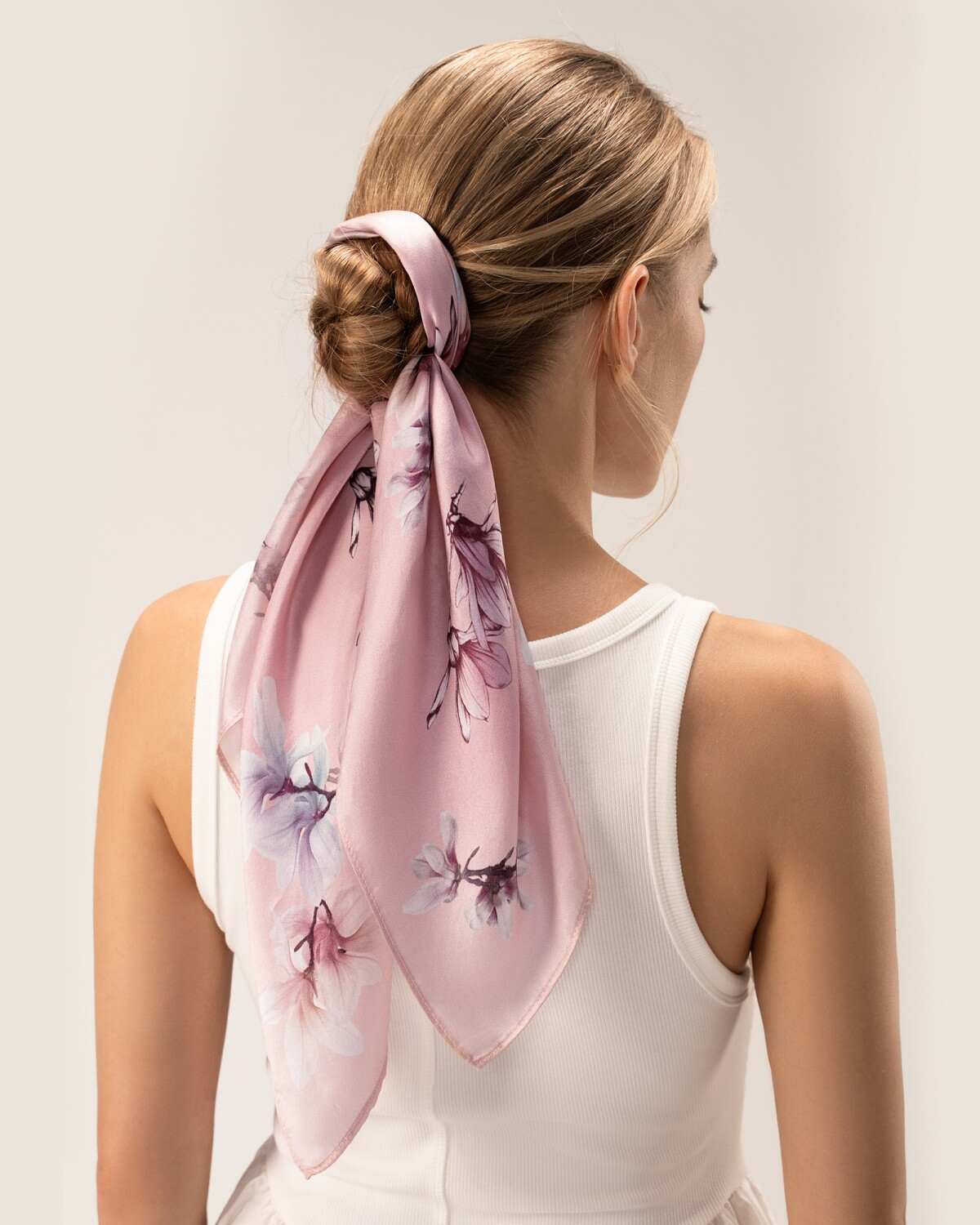A woman dons a floral-patterned silk pink scarf, beautifully complementing her overall look with a touch of sophistication.