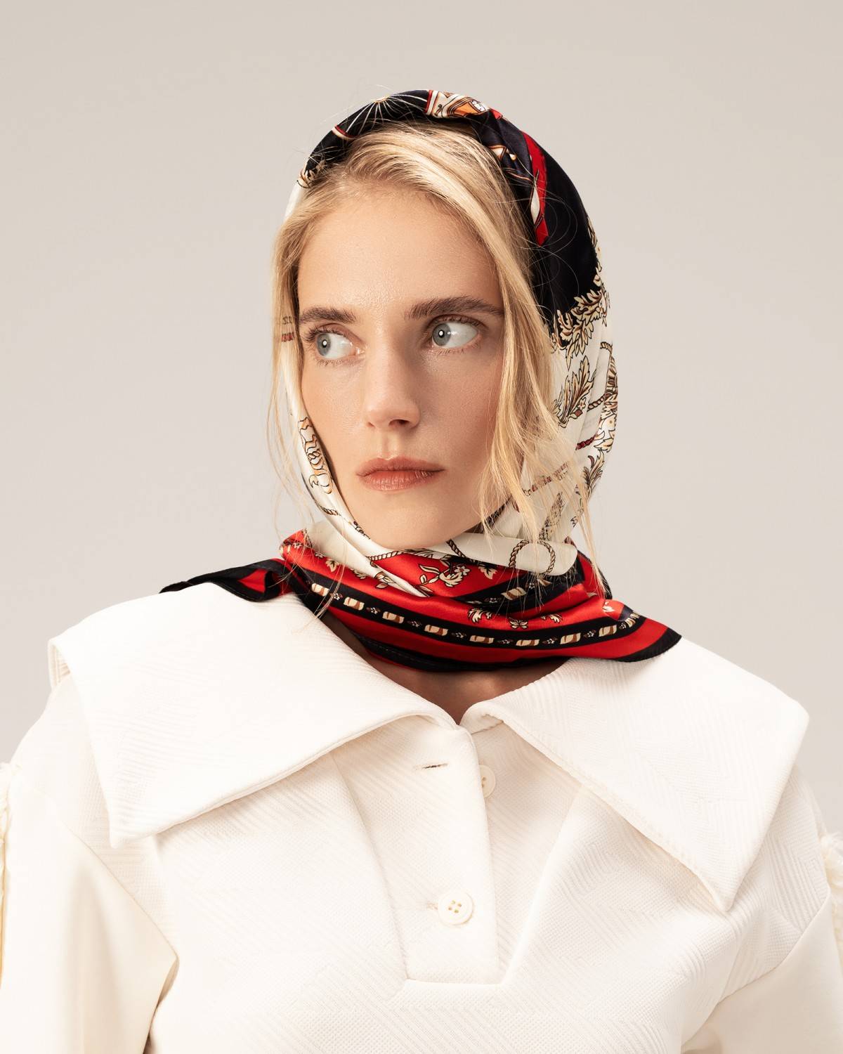 A model in a white top elegantly wears a silk head scarf, showcasing a sophisticated and stylish look.